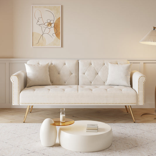 Un divano letto lungo 69,7 pollici rivestito in tessuto di velluto beige, con finiture a borchie e accompagnato da un cuscino coordinato.